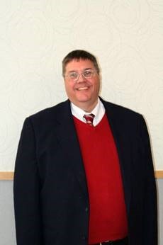 A portrait of Paul Averey wering a red vest, a white collared shirt underneath with a red and yellow tie, and a blue blazer.