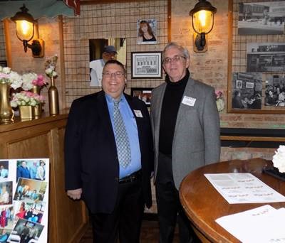 A picture of Paul Avery in a business suit taken at a restauraunt with another gentleman standing to his right, similarly dressed.